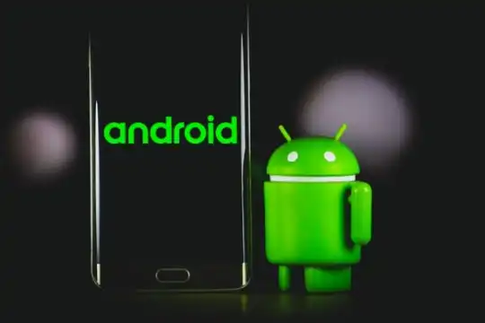 Das Maskottchen von Android neben einem Smartphone mit Android-Logo