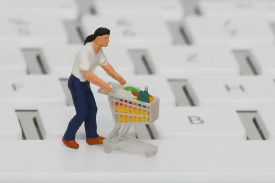 Eine Plastikfigur steht auf einer Tastatur. Eine Figur ist ein Mann, der einen Einkaufswagen voller Lebensmittel hat