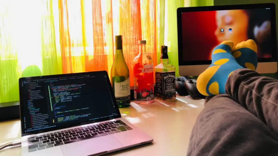 Picture of a laptop displaying a code and a person sitting with their legs crossed on a desk to the side of it