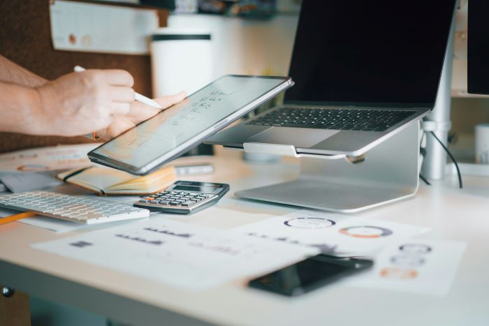 Person holding tablet over desk with laptop, calculator and documents