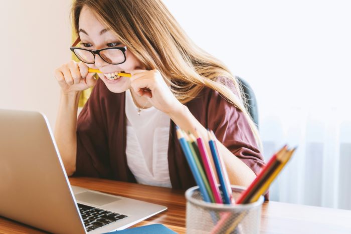 Photo of a woman sitting in front of a laptop clearly frustrated and chewing on a pencil